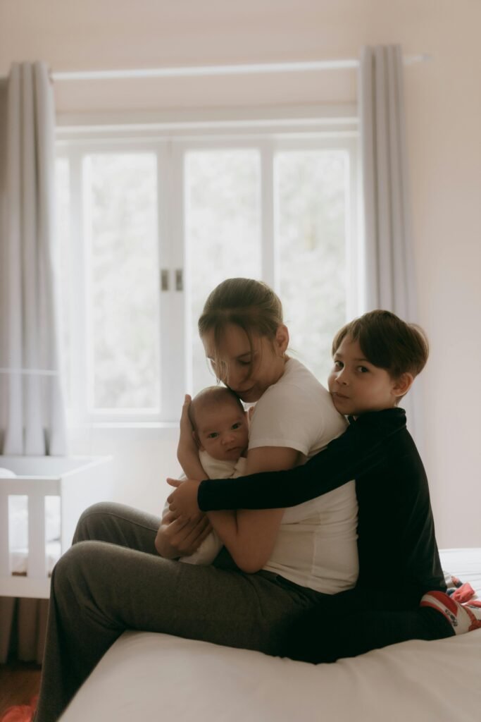 Three siblings embracing warmly on a bed in a cozy, softly lit room.